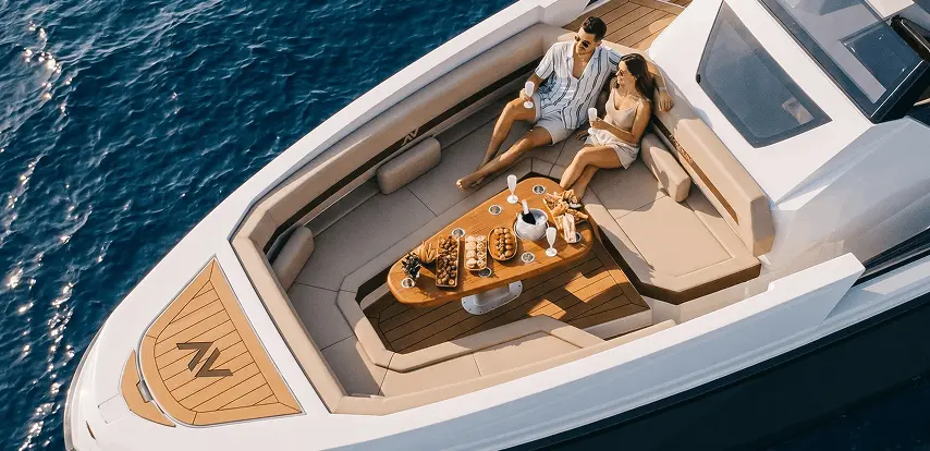 Couple on the Navygon luxury yacht foredeck by Navy Blue, teak table set with food and champagne