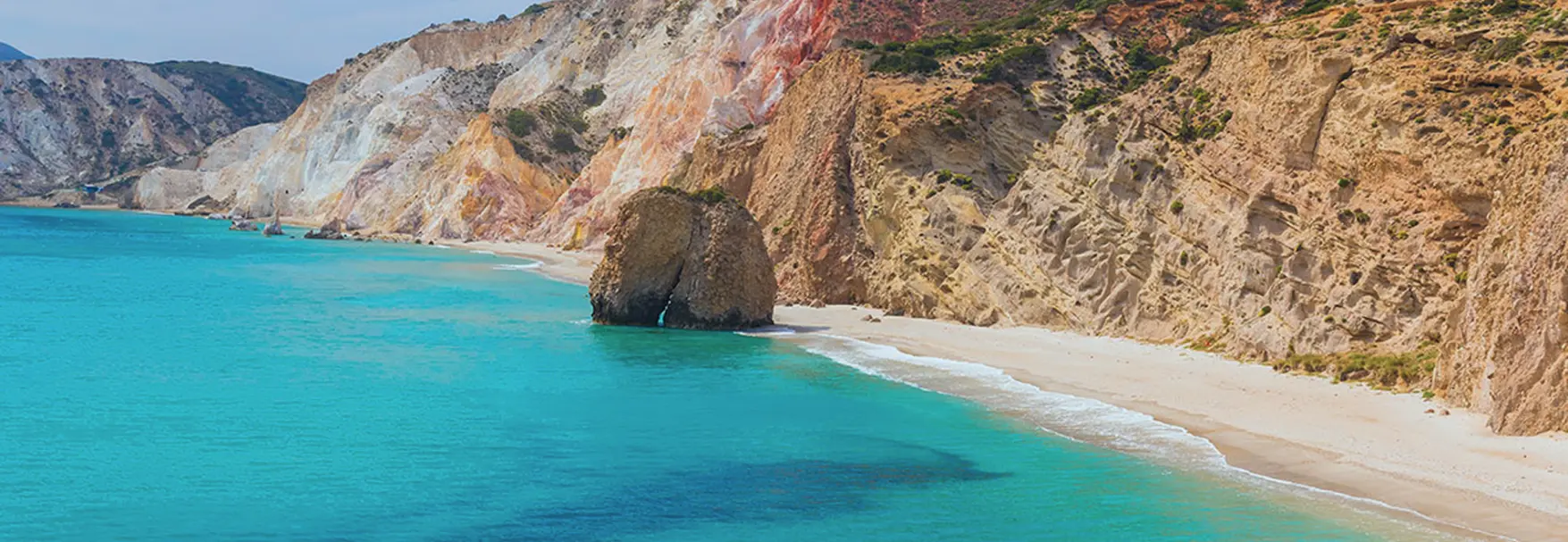 Firiplaka's volcanic shoreline in Milos seen from the sea, with layered cliffs and shallow turquoise water