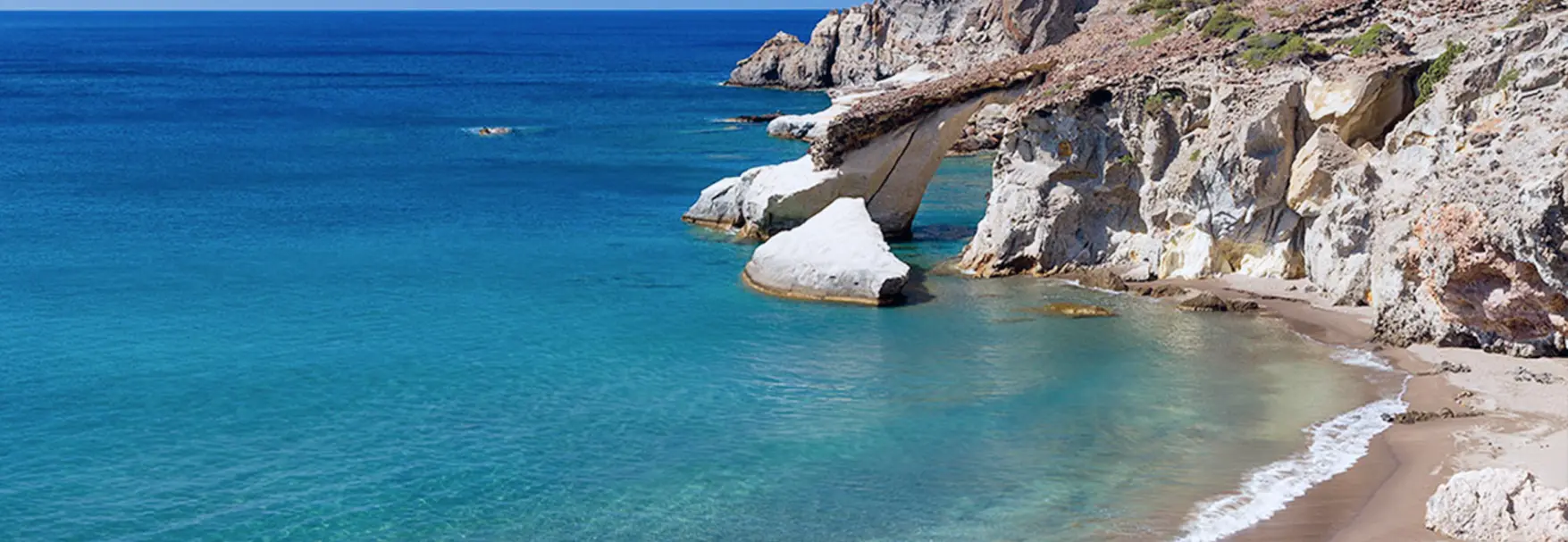 Natural white stone arch over turquoise waters with a sandy cove at Gerontas, Milos