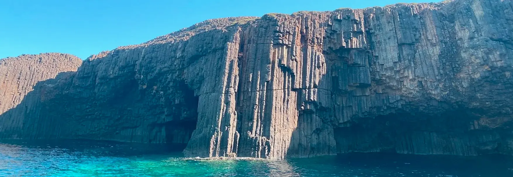 Towering volcanic basalt formations at Glaronisia with crystal-clear turquoise water at their base