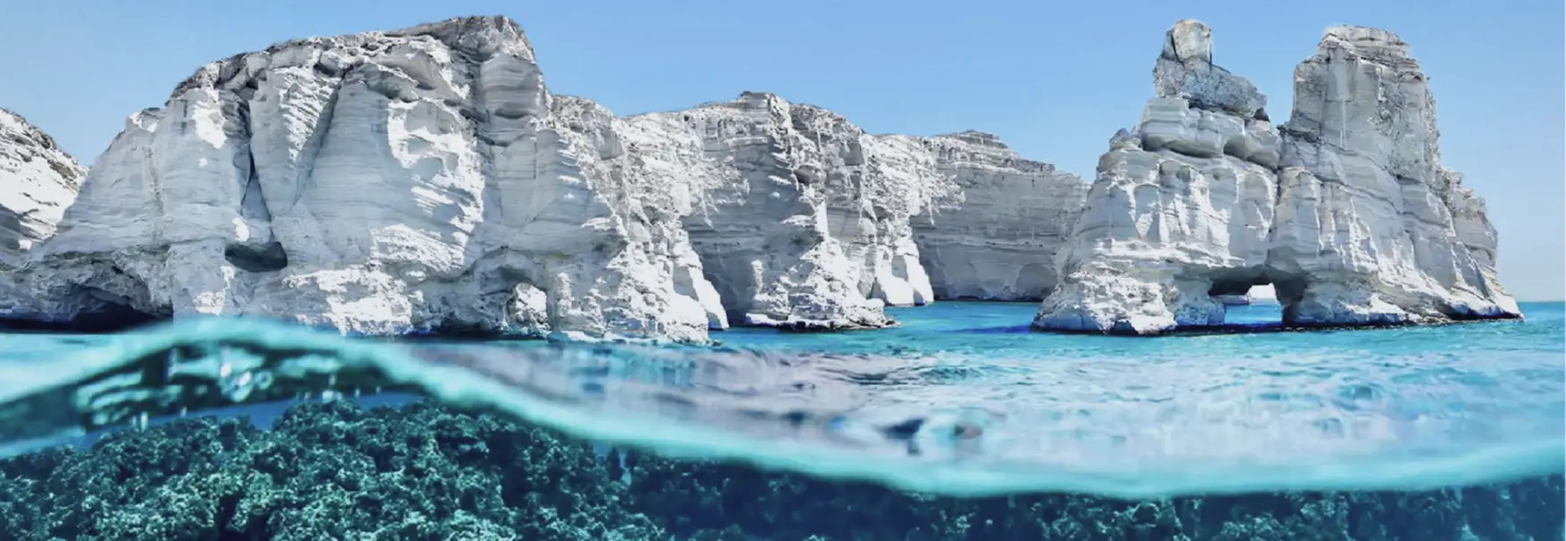 White volcanic cliffs and stone arches at Kleftiko on Milos, turquoise water and seabed visible below the surface