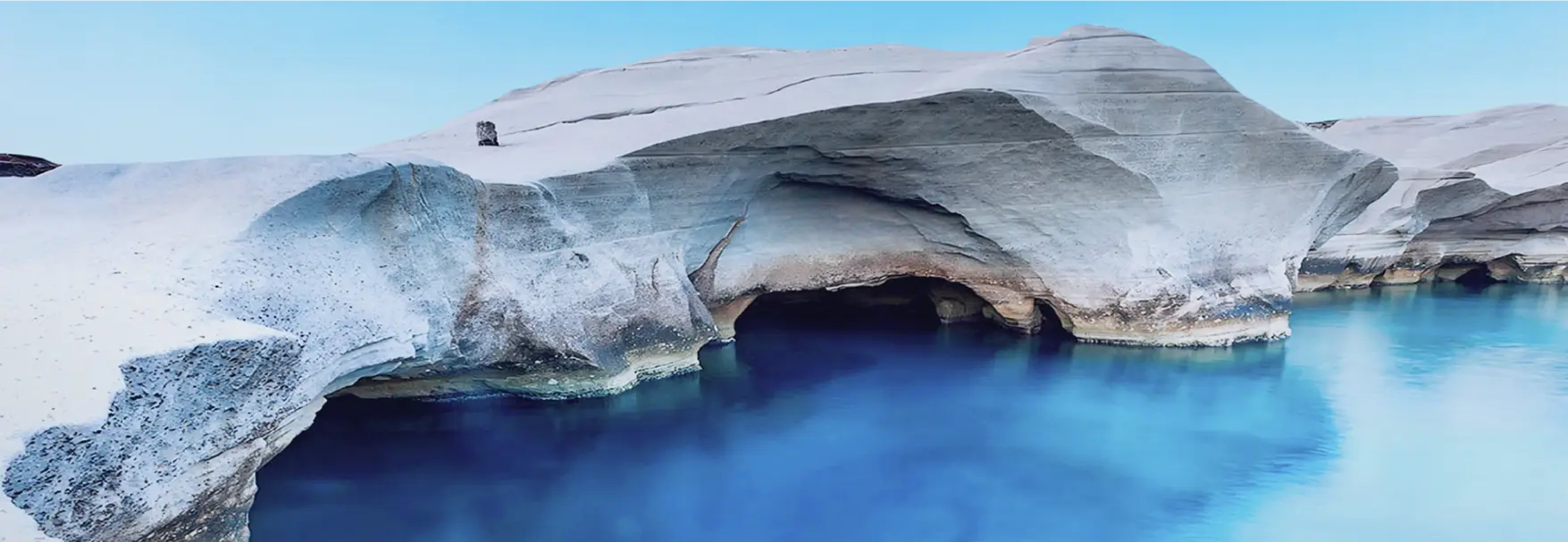 Sarakiniko sea caves and white volcanic cliffs reflecting in vivid blue water, Milos