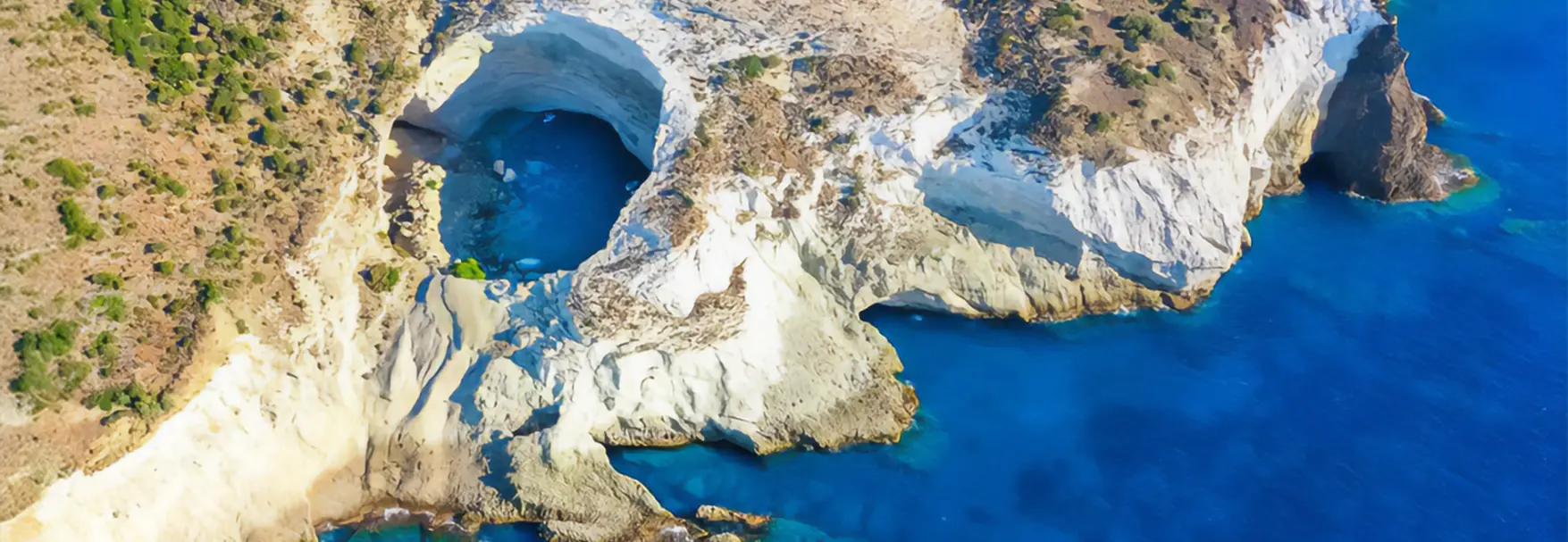 Aerial view of Sikia Cave in Milos showing the circular collapsed roof opening into turquoise sea water