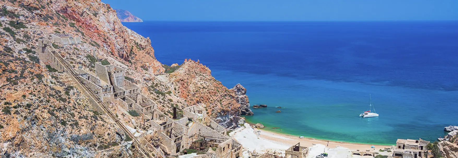Abandoned sulfur mine ruins on ochre cliffs above a yacht anchored in Thiorichia Bay, Milos 