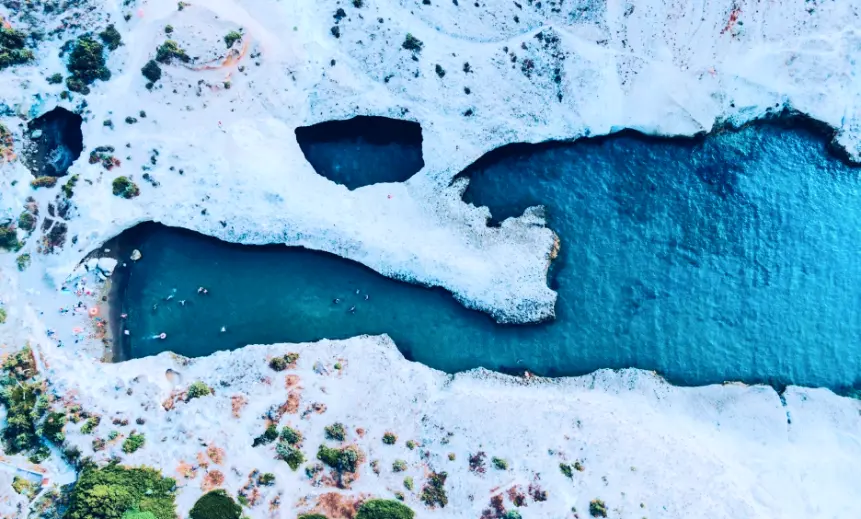 Aerial view of Sarakiniko white rock formations with swimmers in turquoise water, Milos