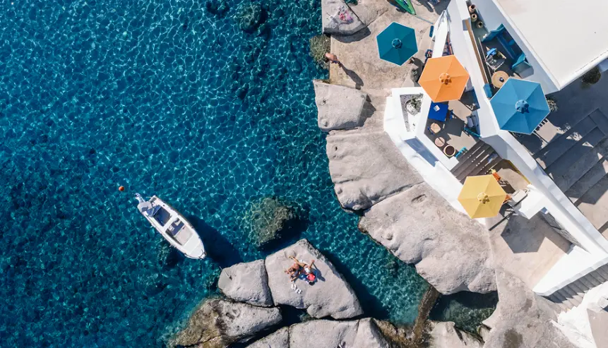 Navy Blue yacht anchored near a rocky Cyclades coastline with guests swimming in turquoise water
