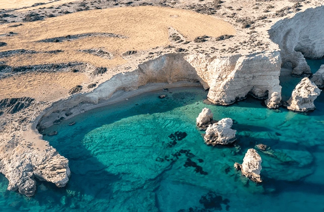Aerial view of white limestone sea caves and a hidden turquoise cove in the Greek Islands