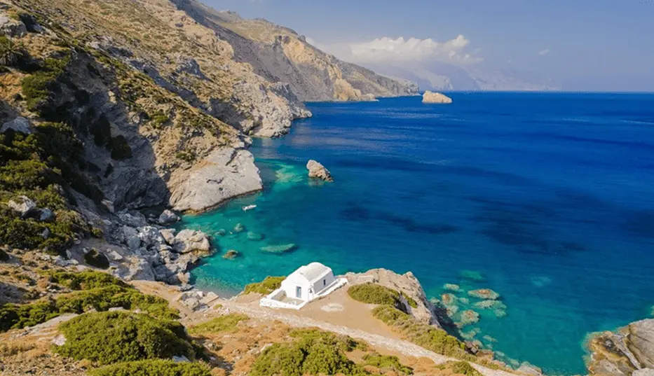 Secluded Cyclades coastline with rocky cliffs, turquoise water, and a small whitewashed chapel