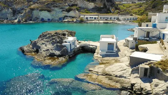 Traditional whitewashed syrmata boathouses built into the rocky shore of Milos over clear turquoise water
