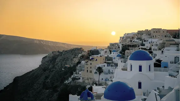 Santorini caldera view at sunset with blue-domed churches and whitewashed buildings on the cliff edge