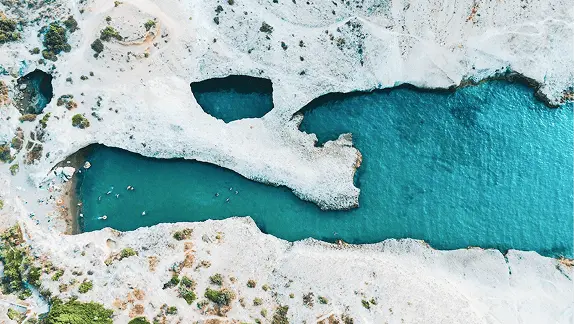 Aerial view of white volcanic rock formations and turquoise sea channels in the Western Cyclades