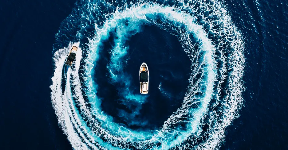 Aerial view of two Navy Blue yachts creating spiral wake patterns in the deep blue Aegean Sea