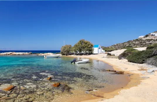 A small chapel above a sandy Antiparos beach, with shallow turquoise water and a moored boat