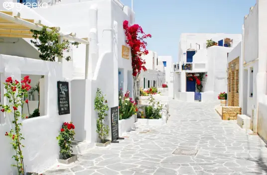 A whitewashed alley in the Chora of Folegandros, with red bougainvillea and taverna tables outside