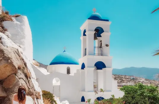 A blue domed church with a white bell tower set against the rocks above the Chora on Ios