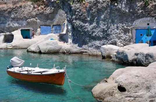 A wooden fishing boat moored beside syrmata boat houses cut into the white rock on Kimolos
