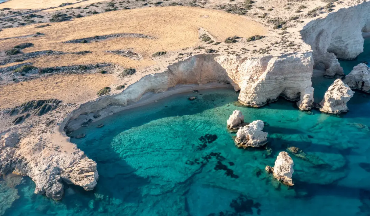 Aerial view of white chalk rock arches and sea stacks surrounding a sandy cove with crystal-clear turquoise water in Koufonisia