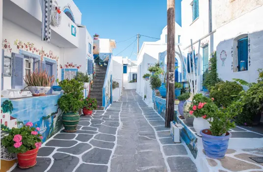 A whitewashed alley on Kythnos with blue doors, painted steps, and flower pots along the walls