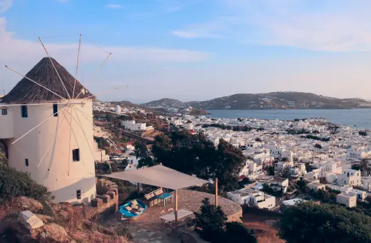 Traditional Mykonos windmill standing above the whitewashed houses of Chora with the Aegean Sea in the distance.