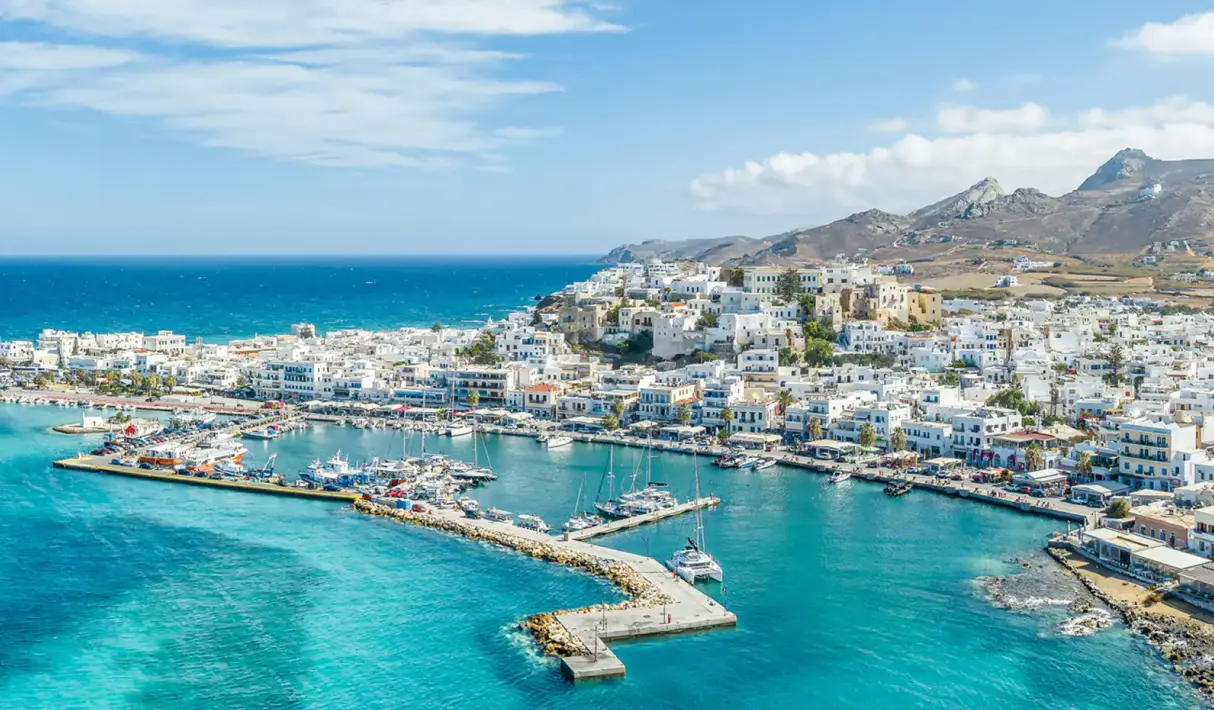 Terraced whitewashed Naxos hillside buildings with a cloth-sailed windmill, warm-toned dome, blue railings, and cascading red bougainvillea