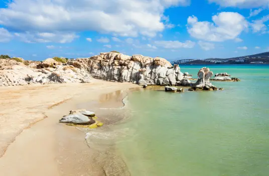 Sculpted granite formations along a Paros beach with turquoise water and golden sand in the Cyclades