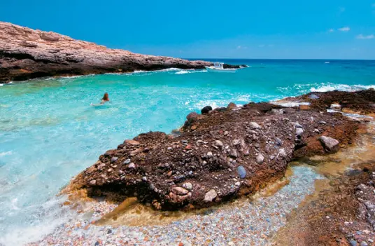 Dark rock shelves and bright turquoise shallows along the rocky shoreline of Sikinos