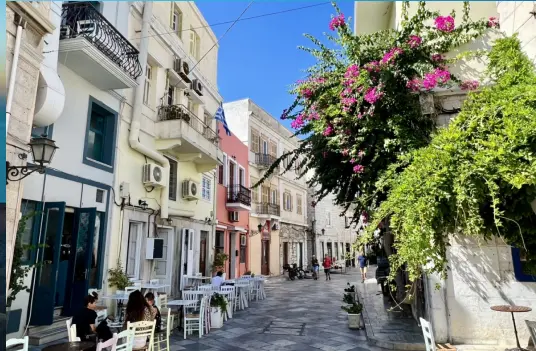 A quiet street on Syros with cafe tables, balconies, and bougainvillea climbing the walls