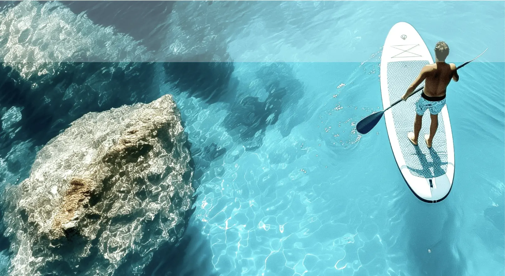 Guest paddle-boarding over crystal-clear turquoise waters in Milos with visible underwater rock formations
