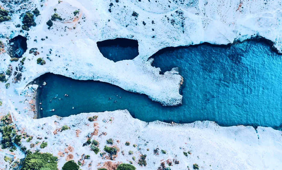 Aerial view of Sarakiniko white rock formations with swimmers in turquoise water – Milos boat tour destination