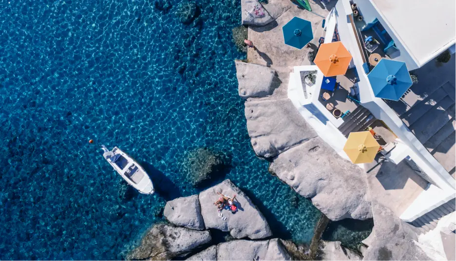 Navy Blue yacht anchored near rocky Cyclades coast with guests swimming – Private Sea Transfer
