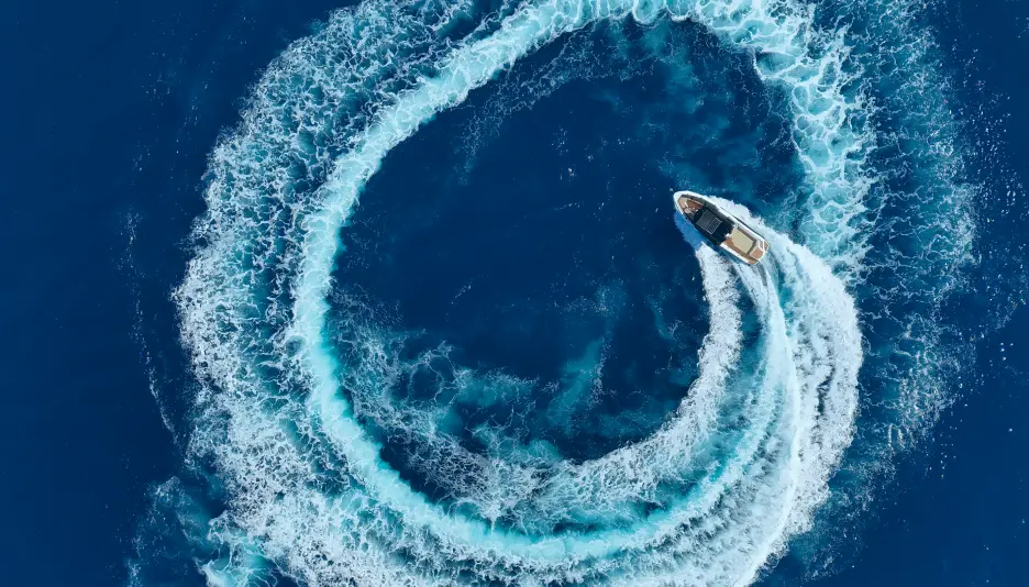 Aerial view of Navy Blue yacht creating spiral wake pattern in the deep blue Aegean Sea – Semi-Private Cruise in Milos