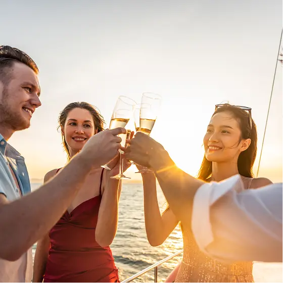 Guests toasting champagne flutes on the deck of a Navy Blue yacht at sunset during a celebration at sea