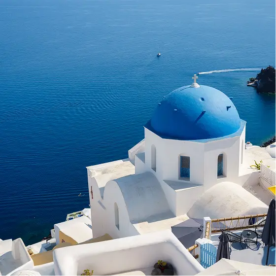 Whitewashed church with a blue dome on a Cycladic hillside above the deep blue Aegean Sea
